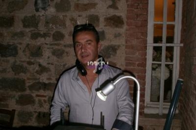 Homme debout derrière une table de mixage, dans une pièce aux murs en pierre avec une fenêtre en arrière-plan.