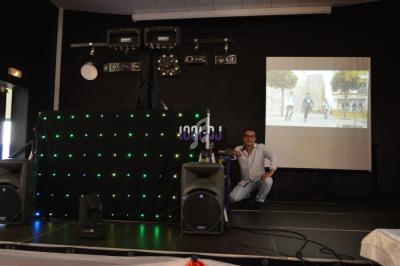 Un homme accroupi près d'une table de mixage devant une scène équipée de lumières et d'un écran de projection.