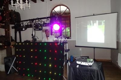 Un DJ anime une soirée dans une salle avec des lumières colorées et un projecteur affichant une image.