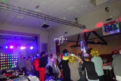 Des personnes dansent sous des lumières colorées dans une salle décorée pour une fête sur le thème des années 80.