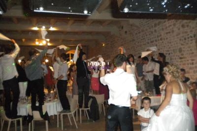 Des invités dansent sur des chaises et agitent des serviettes lors d'une fête dans une salle en pierre.