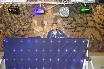 Un DJ mixant derrière une table éclairée de lumières LED violettes, avec un mur décoratif en arrière-plan.