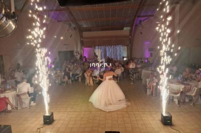 Un couple danse au centre d'une salle de réception décorée, entouré de gerbes d'étincelles et d'invités assis.