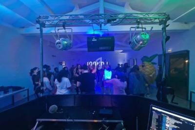 Vue depuis une cabine de DJ sur une piste de danse éclairée, avec des participants et des jeux de lumière colorés.