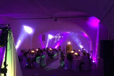 Salle voûtée éclairée de lumières colorées, avec des invités assis à des tables décorées pour un événement festif.