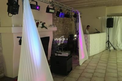 Installation d'éclairage et matériel de sonorisation dans une salle avec un DJ en arrière-plan.