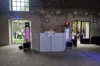 Installation de DJ dans une salle en pierre avec une table blanche, des enceintes et des lumières colorées.