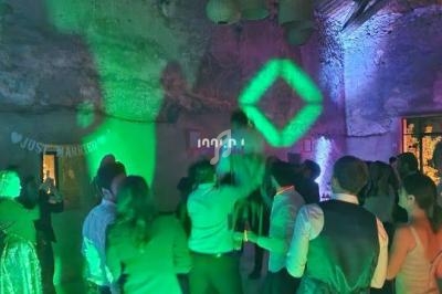 Personnes dansant sous des lumières colorées dans une salle en pierre avec des décorations suspendues.