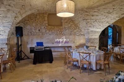 Salle en pierre avec tables rondes dressées pour un événement, éclairée par une suspension centrale.