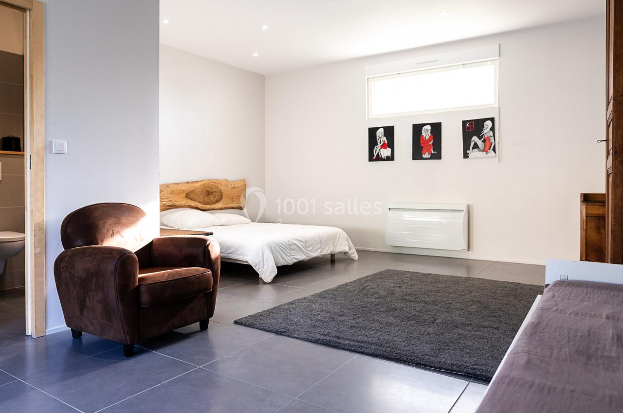 Chambre lumineuse avec lit double, fauteuil en velours marron, tapis gris et décorations murales modernes.