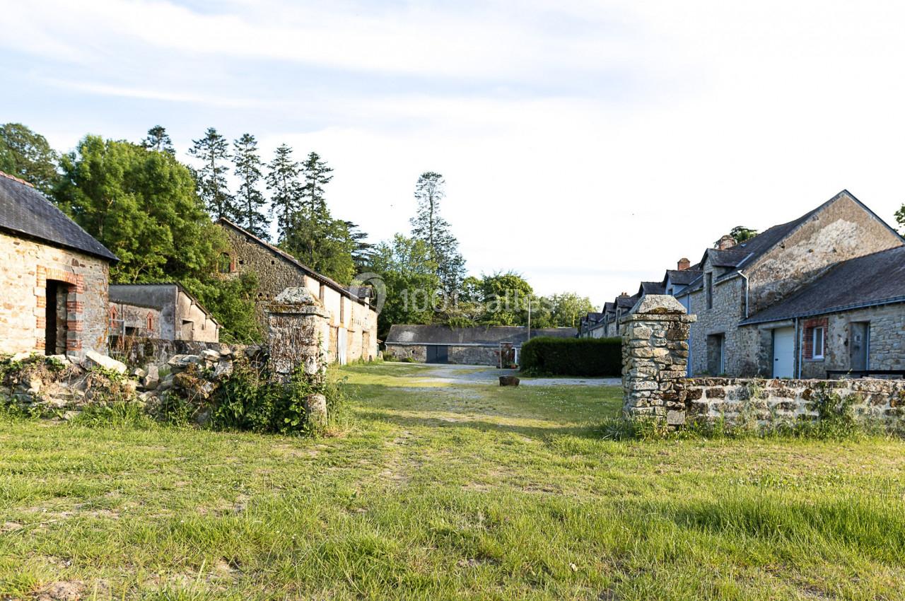 Cour d'une ancienne ferme en pierre avec bâtiments traditionnels, entourée de verdure et d'arbres.