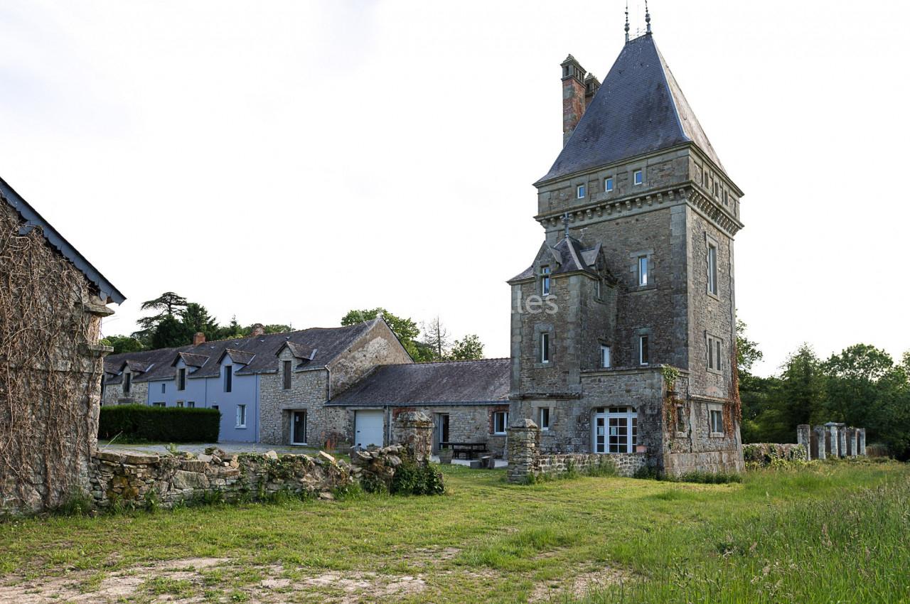 Grande maison en pierre avec une tour, entourée de verdure et d'un mur en pierre dans un cadre rural.