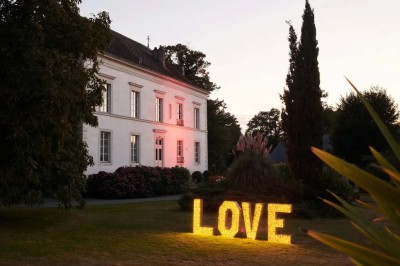 Pelouse verdoyante entourée de grands arbres sous un ciel partiellement nuageux.