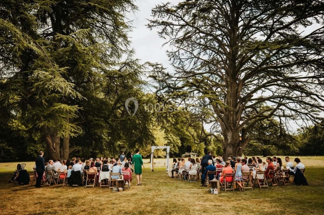Cérémonie en plein air avec des invités assis sur des chaises, entourés d'arbres dans un cadre naturel.