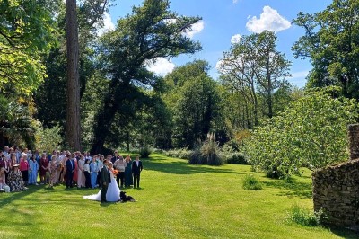 Pelouse verdoyante entourée de grands arbres sous un ciel partiellement nuageux.