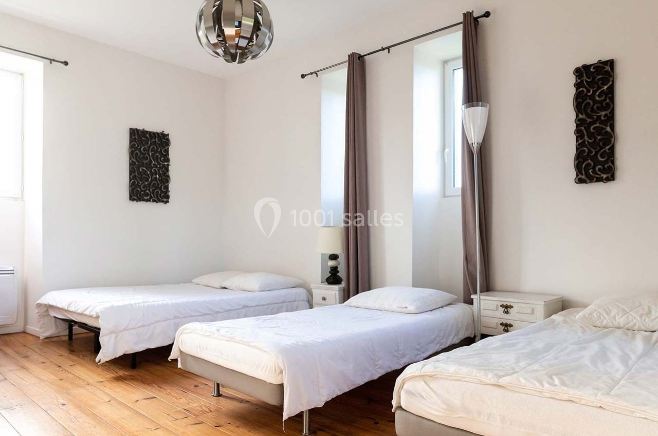 Chambre lumineuse avec trois lits simples, parquet en bois, murs blancs et décoration murale sobre.