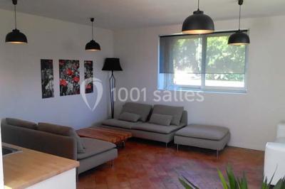 Étang calme entouré d'arbres avec un bâtiment blanc visible en arrière-plan sous un ciel bleu.