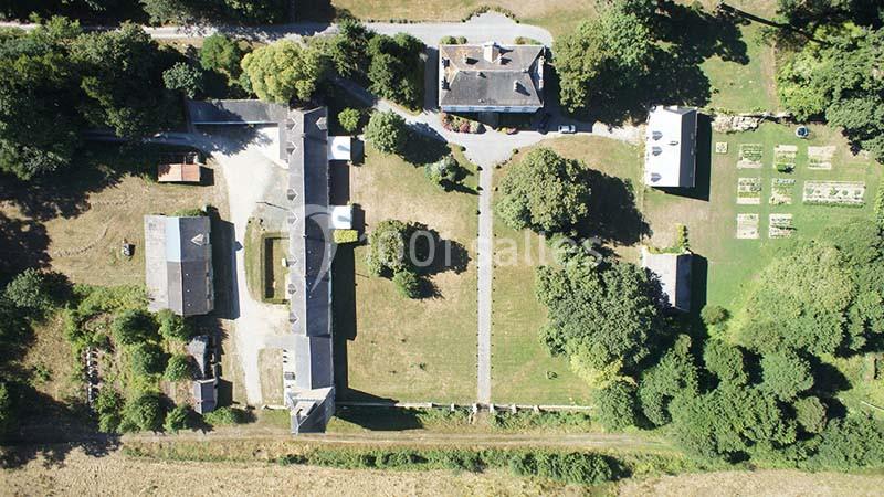 Vue aérienne d'un domaine rural avec bâtiments en pierre, jardin, allées et espaces verts entourés d'arbres.