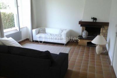 Étang calme entouré d'arbres avec un bâtiment blanc visible en arrière-plan sous un ciel bleu.