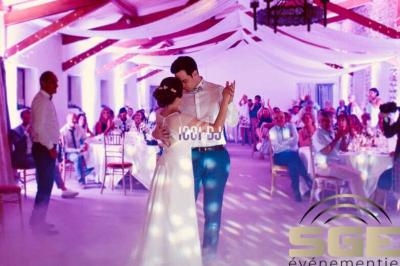 Un couple danse au centre d'une salle décorée pour un mariage, entouré d'invités assis à des tables.