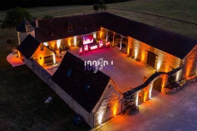 Vue aérienne d'une grande bâtisse en pierre éclairée par des lumières chaudes, entourée de pelouses.