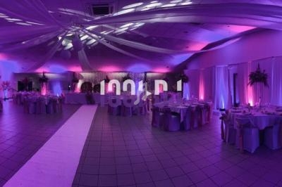 Salle de réception décorée avec des tables dressées, éclairage violet et plafond orné de voilages blancs.