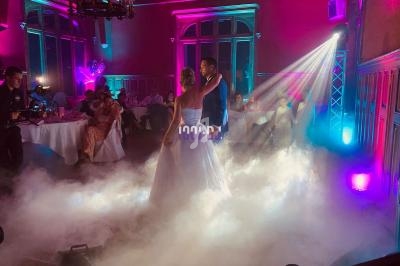 Un couple danse au milieu d'une piste entourée de fumée, éclairée par des lumières colorées dans une salle festive.