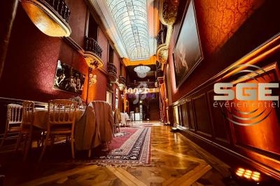 Salle élégante avec parquet, tables dressées, murs rouges ornés de tableaux et plafond vitré majestueux.