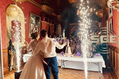 Un couple de mariés regarde un gâteau de mariage illuminé par des fontaines d'étincelles dans une salle élégante.