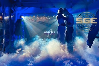 Un couple danse dans une ambiance lumineuse bleutée avec des effets de fumée et des guirlandes en arrière-plan.