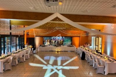 Salle de réception décorée avec des guirlandes lumineuses, tables dressées et éclairage chaleureux.