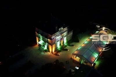 Vue aérienne nocturne d'un bâtiment éclairé par des lumières colorées, avec une structure couverte adjacente.