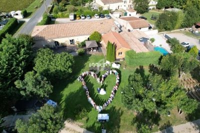Vue aérienne d'un groupe de personnes formant un cœur sur une pelouse, entouré de bâtiments et de verdure.