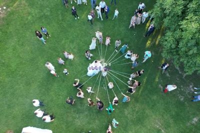 Vue aérienne d'un groupe de personnes sur une pelouse, tenant des rubans attachés à un point central.