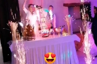 Des serveurs présentent une pièce montée illuminée par des fontaines d'étincelles dans une salle de réception festive.