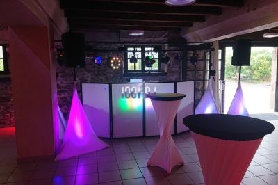 Installation de matériel de sonorisation et éclairage dans une salle avec tables hautes et décor lumineux.