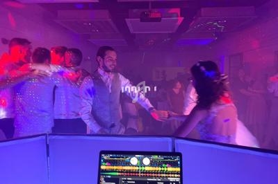 Des invités dansent et s'amusent sous des lumières colorées lors d'une fête avec un DJ en arrière-plan.