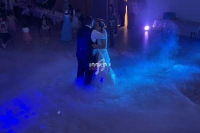 Un couple danse au milieu d'une piste enveloppée de fumée et éclairée par une lumière bleue dans une salle sombre.