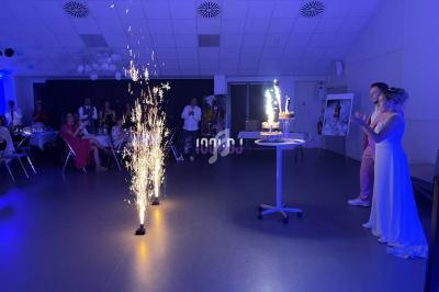 Un couple observe un gâteau d'anniversaire ou de mariage avec des cierges étincelants dans une salle éclairée en bleu.