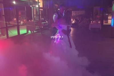 Un couple danse dans une salle faiblement éclairée, entouré de fumée et de lumières colorées.