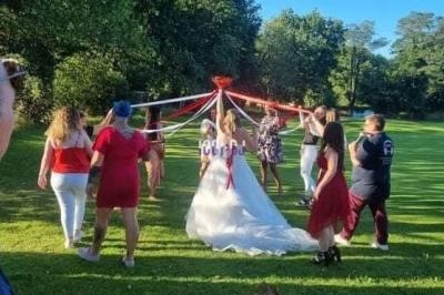 Des personnes entourent une mariée sous un ciel bleu, tenant des rubans colorés dans un parc verdoyant.