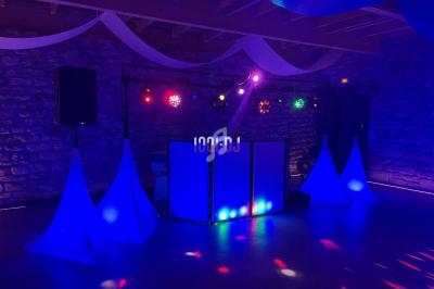 Installation lumineuse de DJ avec éclairages colorés et décorations blanches dans une salle en pierre.