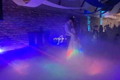 Un couple danse dans une salle éclairée par des lumières colorées, entourée de fumée au sol.