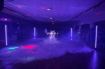 Un couple danse au centre d'une piste entourée de fumée et éclairée par des lumières colorées.