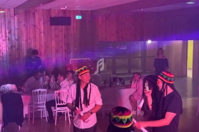 Des personnes dansent et discutent dans une salle éclairée de lumières colorées, certaines portant des bonnets rasta.