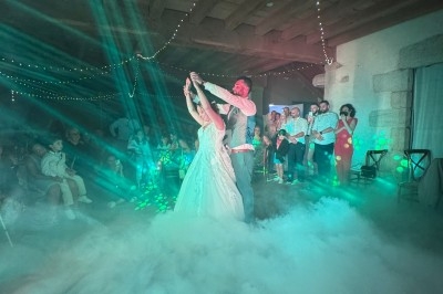 Un couple danse sous des lumières colorées et des effets de fumée, entouré d'invités dans une salle festive.