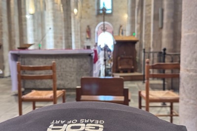Intérieur d'une église avec des chaises en bois, un autel et une voûte en pierre illuminée par la lumière naturelle.