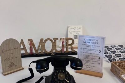 Téléphone rétro noir sur une table décorée avec des objets, dont un panneau ’AMOUR’ et un livre d'or numérique.
