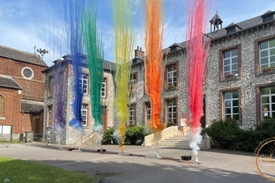Jets de poudre colorée s'élevant devant un bâtiment en pierre avec des fenêtres et une cour pavée.