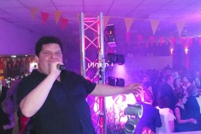 Un chanteur anime une soirée festive dans une salle décorée de guirlandes colorées, avec un public en arrière-plan.